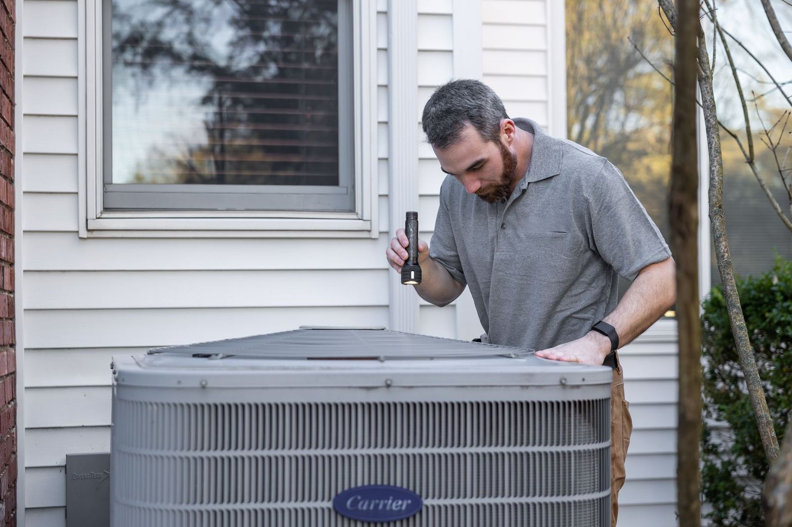 HVAC technician checking a newly installed outdoor condenser unit beside a house